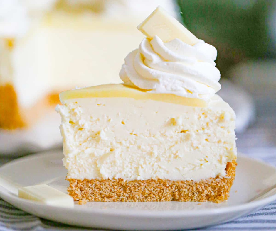 Decadent white chocolate cheesecake slice featuring a golden graham crust, smooth cream cheese filling, and elegant white chocolate garnish. Easy holiday recipe.